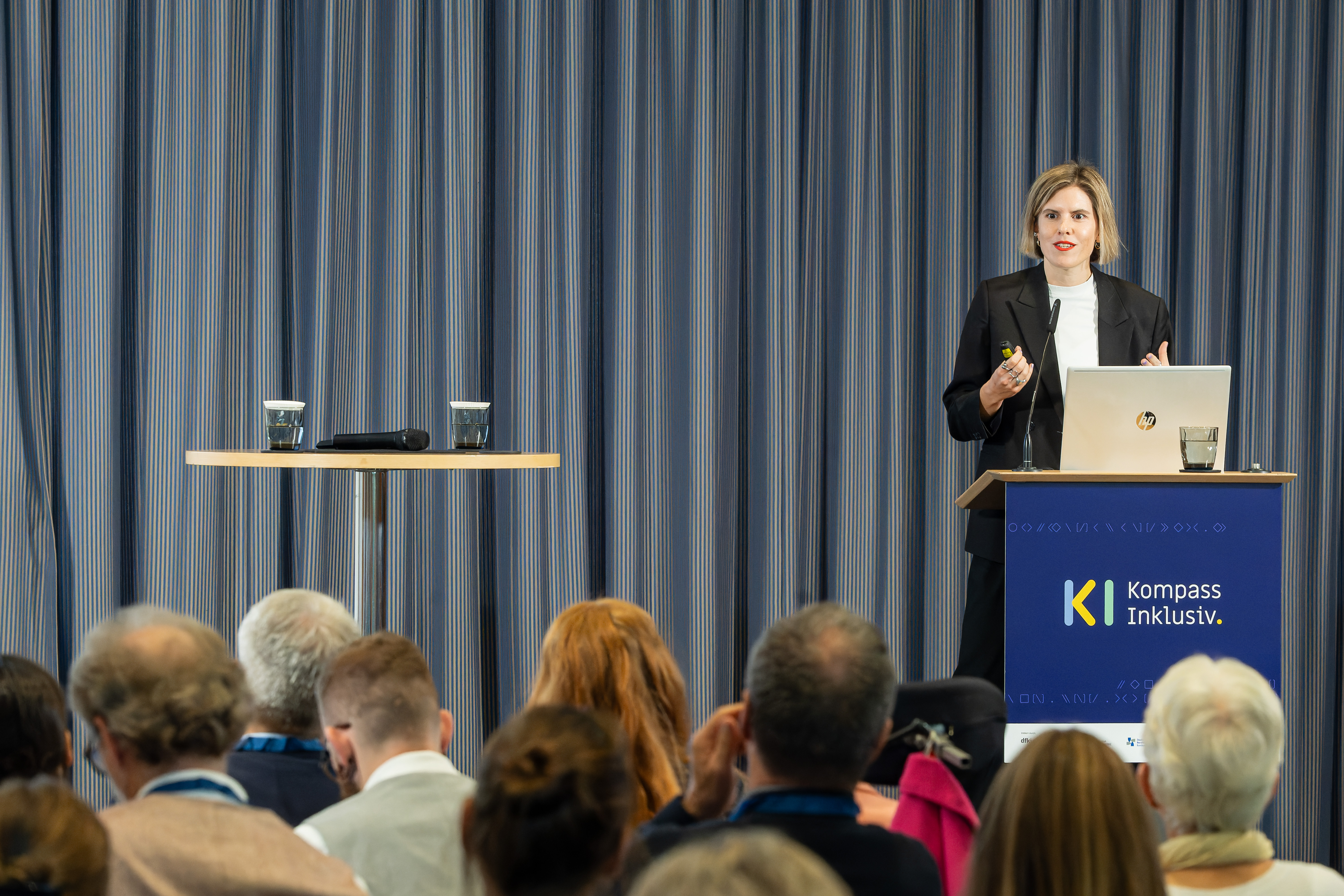 Foto von Hannah Ruschemeier, die gerade am Rednerpult mit der Aufschrift "KI Kompass Inklusiv" spricht.