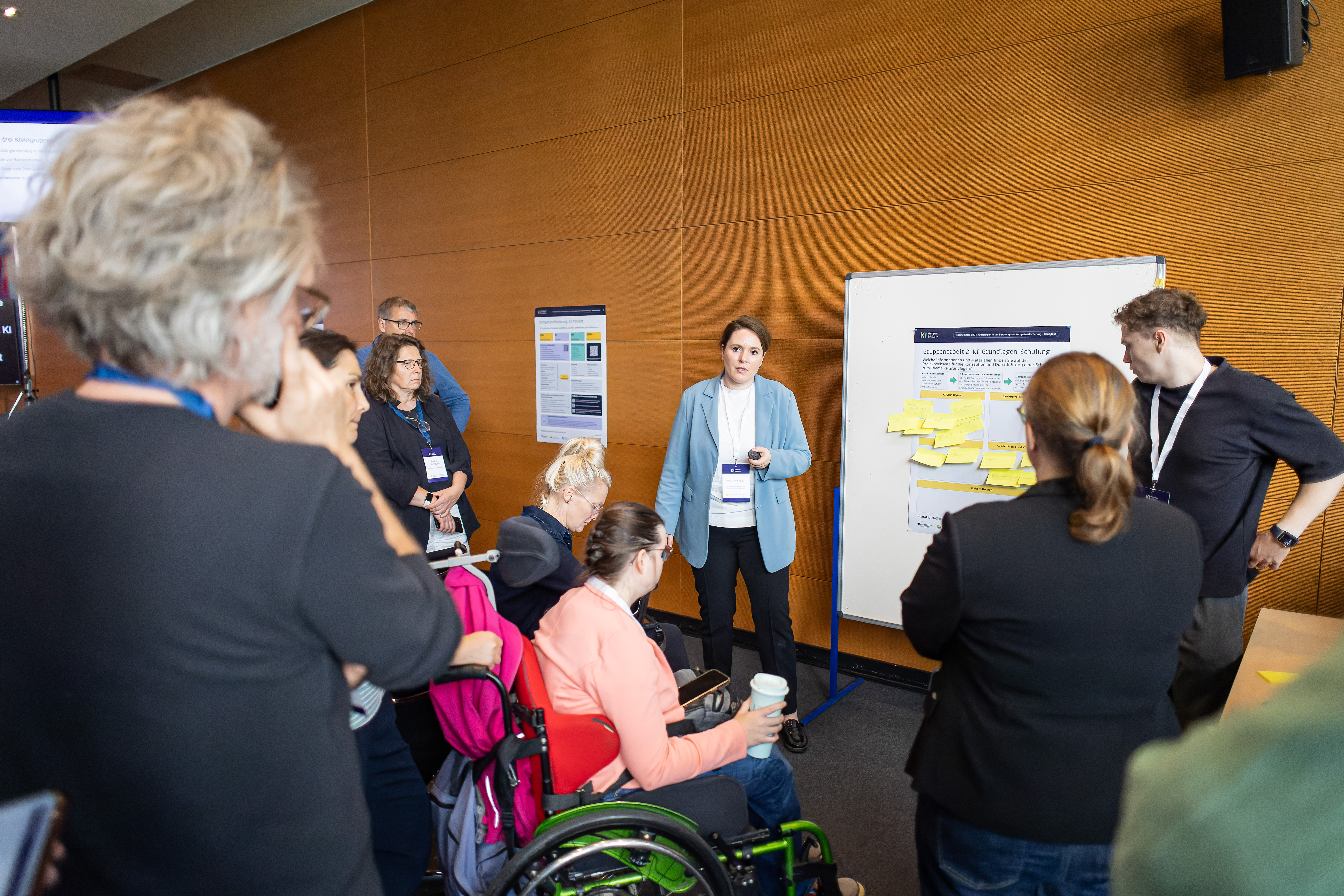 Foto von einer kleinen Gruppe vor einem Flipchart. Eine Moderatorin steht ihnen zugewandt und sagt etwas.